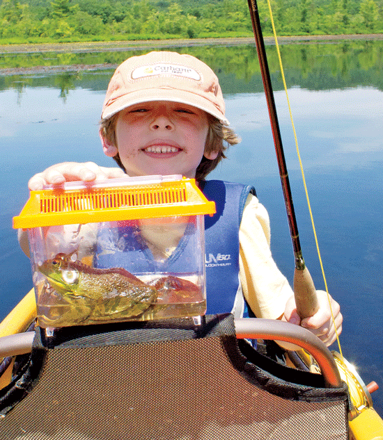 A boy with a fly rod in one hand and a frog in a plastic aquarium in the other.
