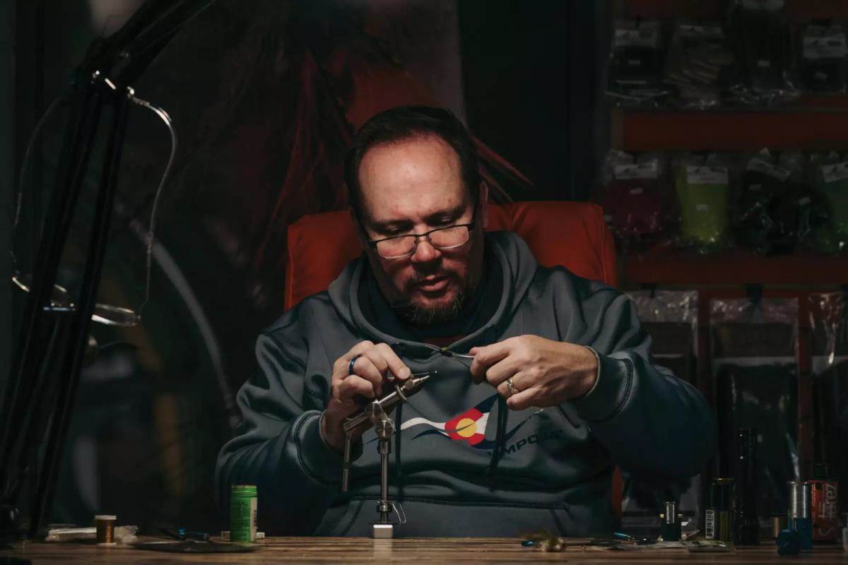 Charlie Craven sitting at his desk tying a fly. 
