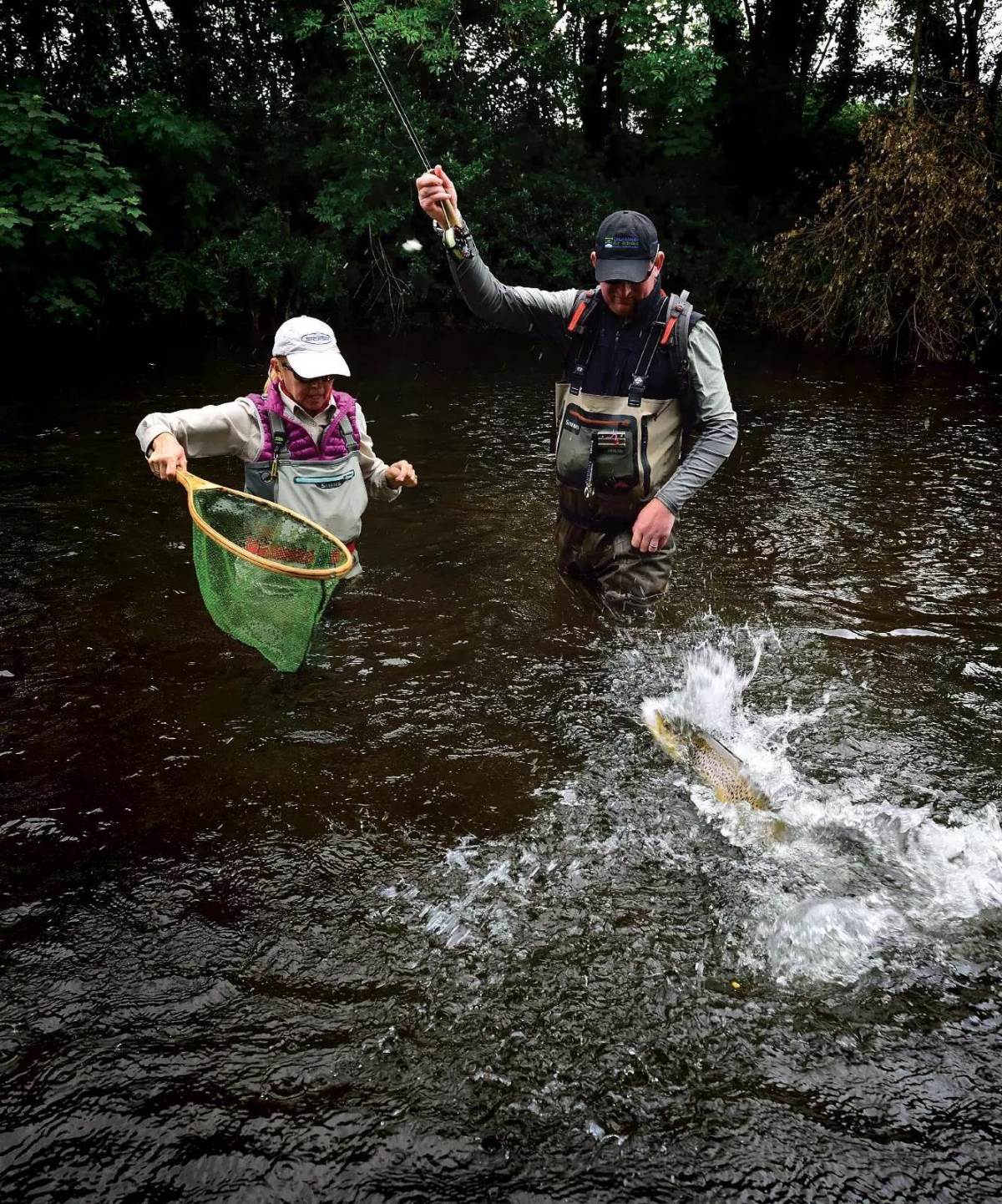 A fly angler landing an Atlantic salmon next to his partner about to net it. 