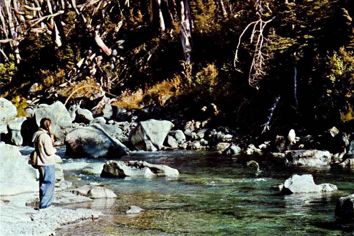 A fly angler hooked up to a leaping trout in a jade-green rocky river.