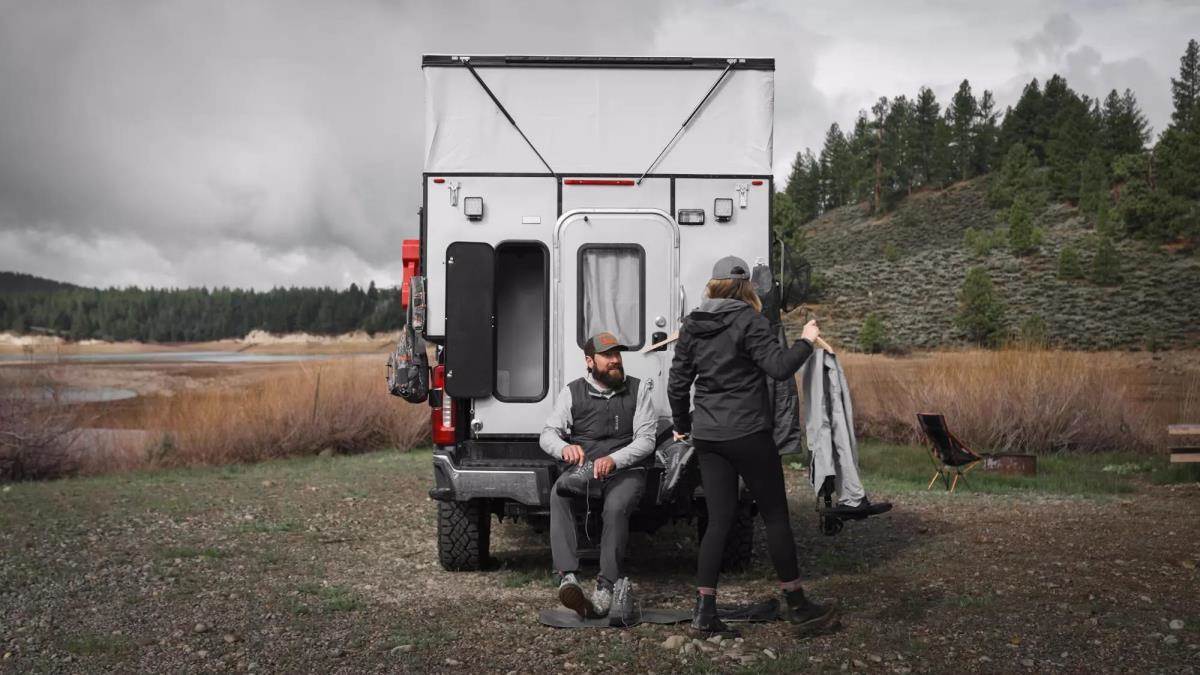A man and a woman taking their fishing gear off next to a popup truck camper. 
