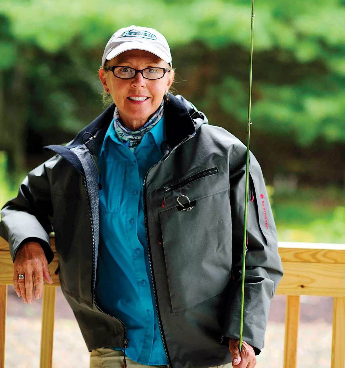 Cathy Beck smiling for the camera, holding a fly rod. 