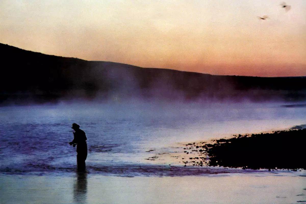 A silhouetted fly angler fishing a steamy river at sunrise. 