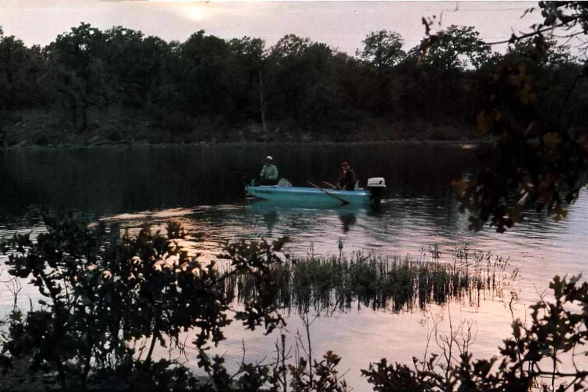 A boat with two anglers on a weedy lake during low light. 