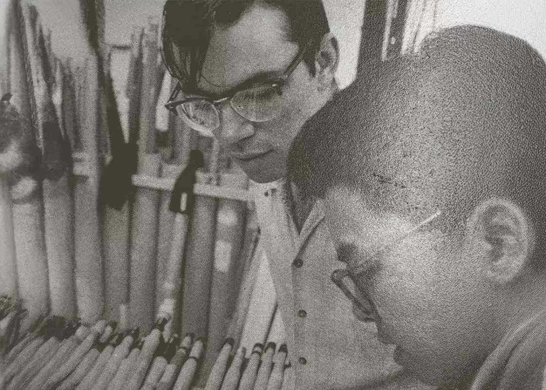 Two men examining a pile of fly rods. 