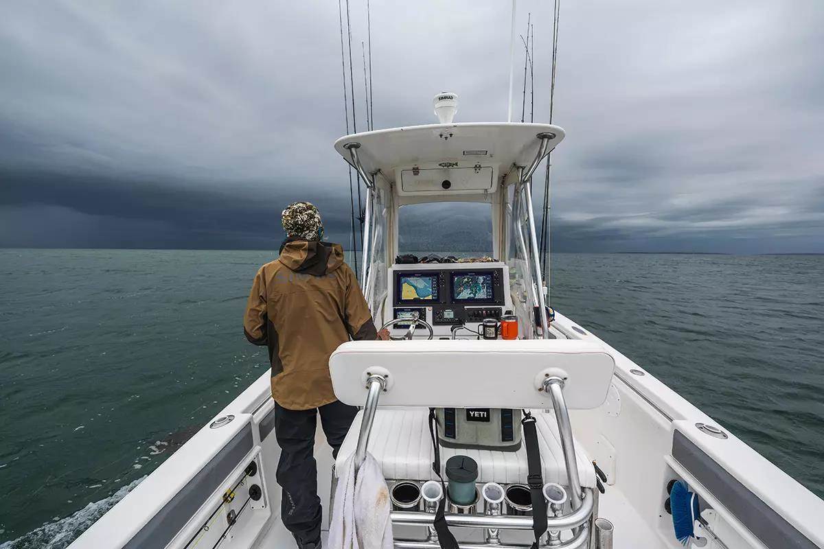 An angler standing on the deck of a boat heading into stormy skies. 