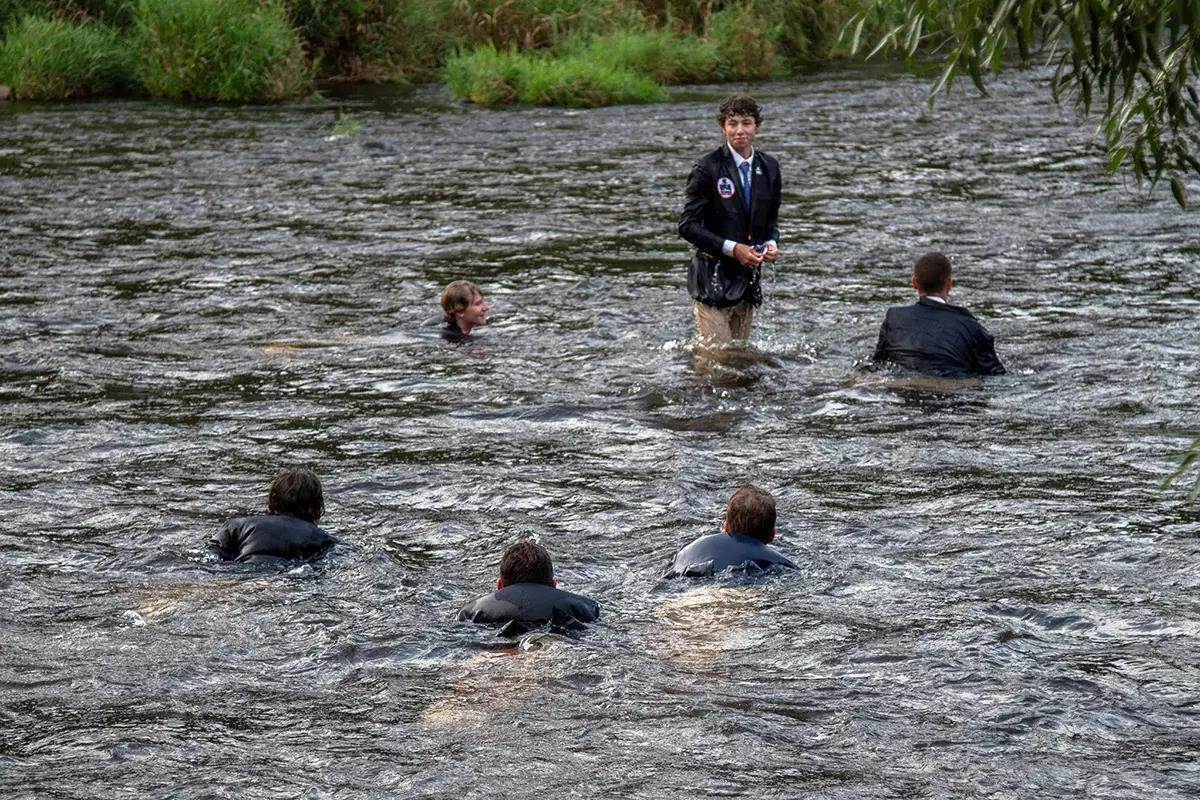 Six young men in blue sport coats swimming in a river. 