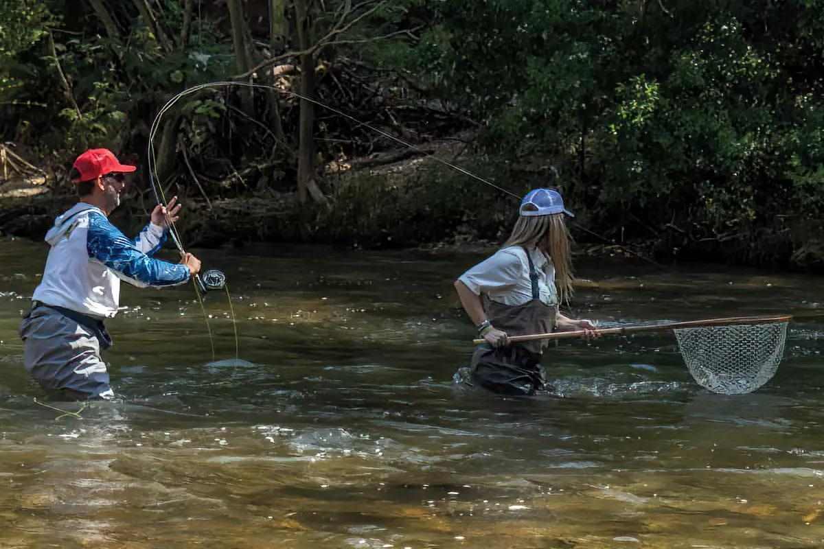 A fly angler fighting a fish with his netwoman at the ready.