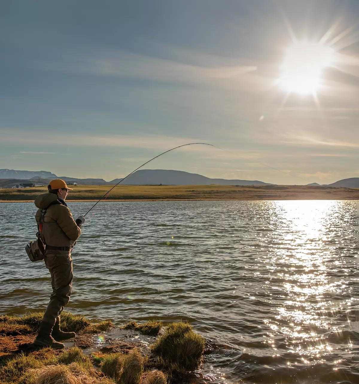 A fly angler hooked up to a fish under a bright sun. 