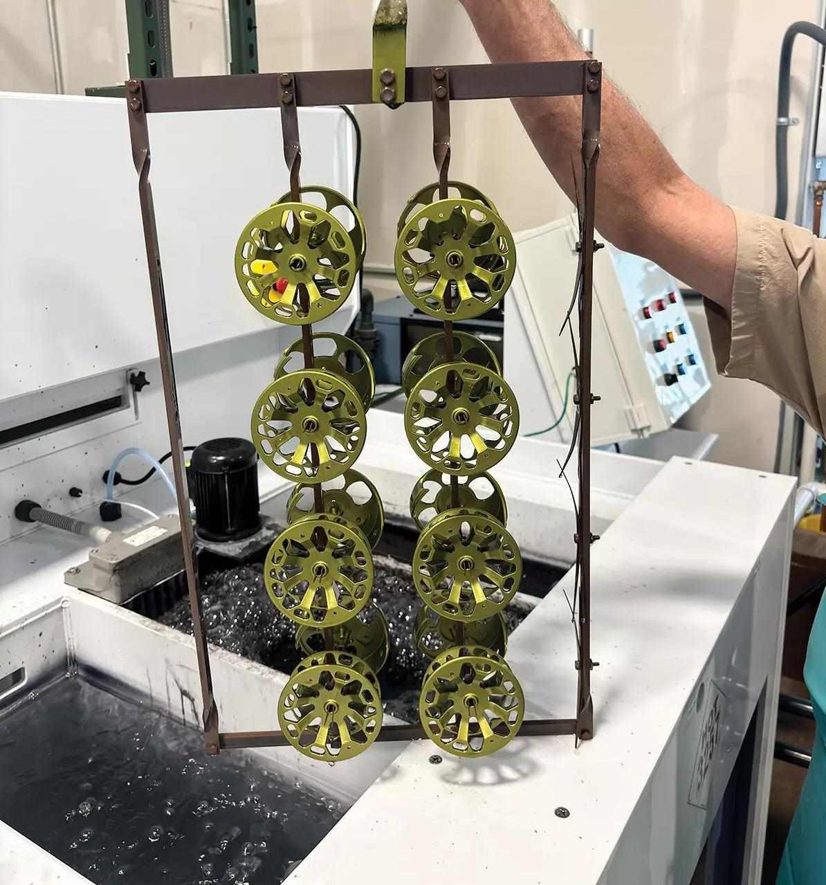 An arm holding a rig that holds eight fly reels for dipping them into an acid solution to anodize them.