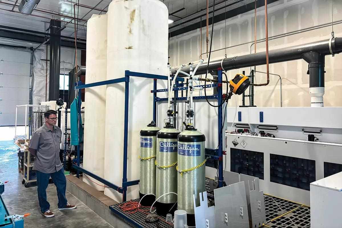 A man in a warehouse looking at various cylinders with attached tubes. 