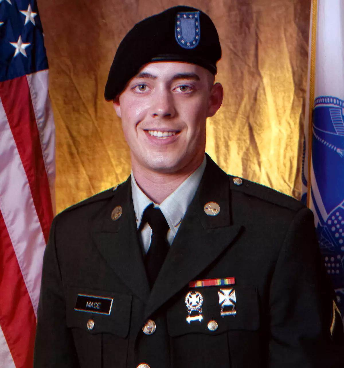 A portrait photo of Army SPC Stephan Lee Mace in full uniform in front of flags.