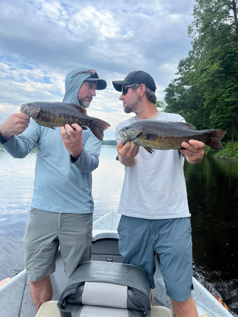 Two anglers standing in a boat holding smallmouth bass